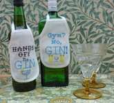 Click/tap for more details of Gin Bottle Aprons - Gym and Hands Off (cross stitch) by Julie Lynes